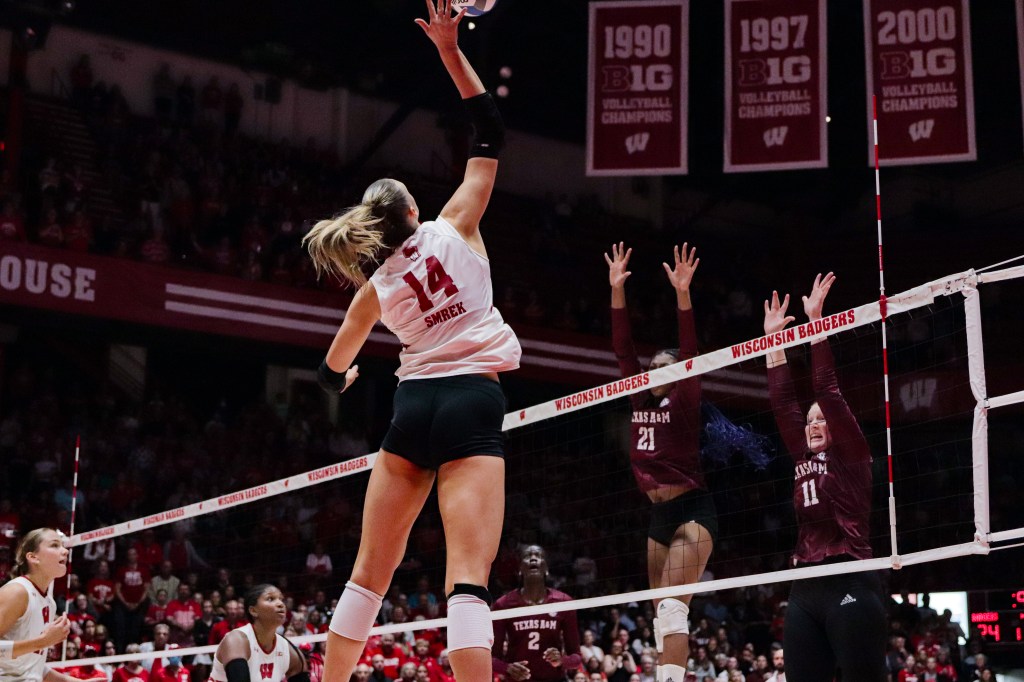 Anna Smrek hits a ball while two defenders jump on the other side of the net.