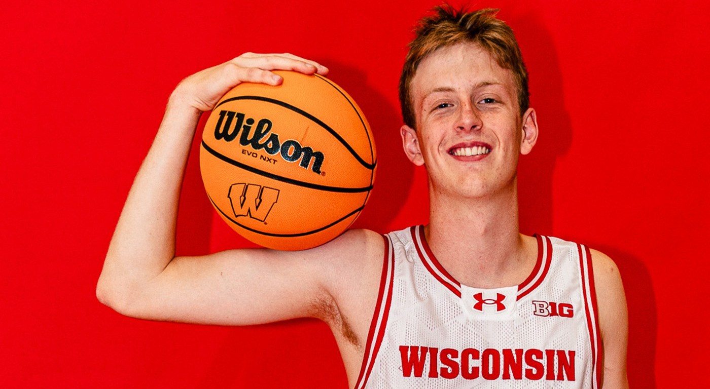 Jack Robison stands in front of a red background, holding a basketball in his arm.