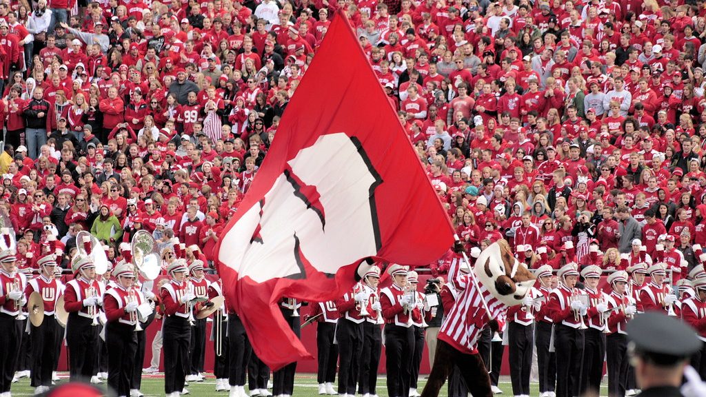 Bucky Badger runs across the field with a "W" flag.