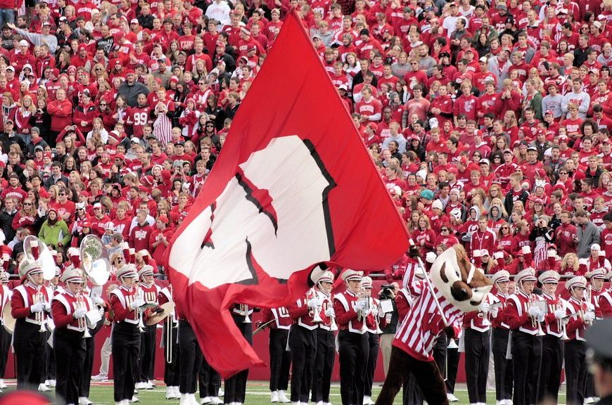 Bucky Badger runs across the field with a "W" flag.
