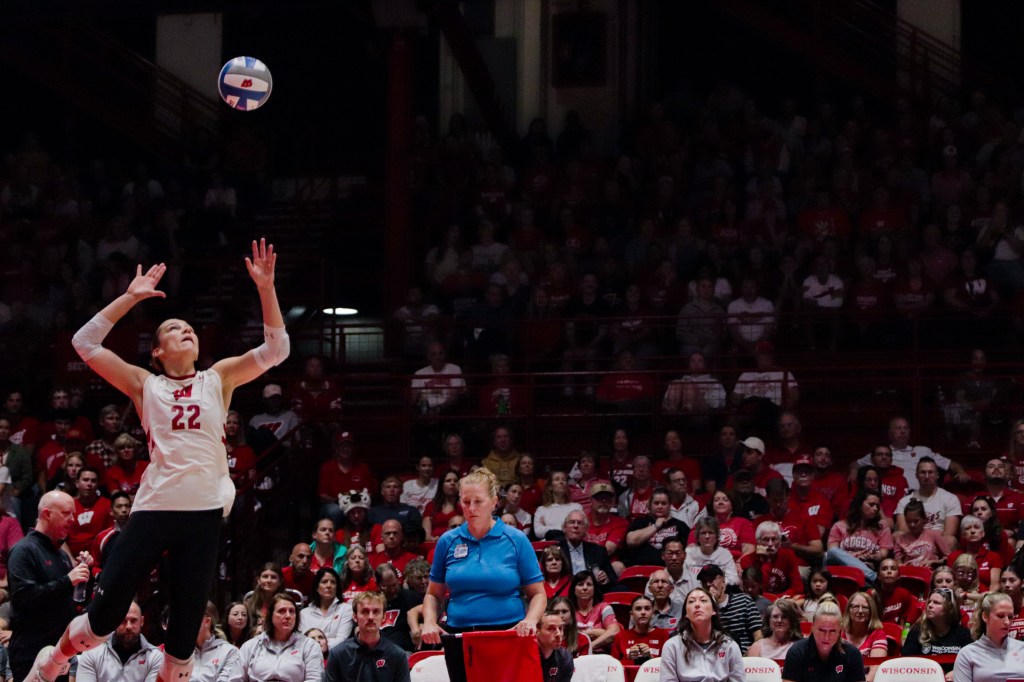 Julia Orzol jumps in the air with the ball above her while a referee in a blue shirt stares at the ground.